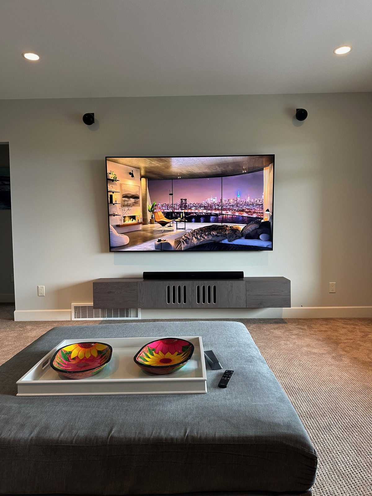 TV with a Sonos Arc soundbar and on-wall surround speakers over a floating cabinet